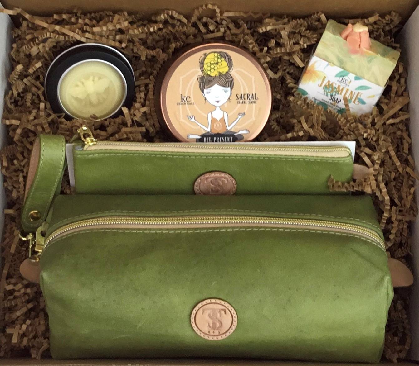Town & Shore Handcrafted Serenity Gift set featuring T5 Leather bath kit and brush bag shown in bright green calfskin leather. KC Essentials artisan made vegan bar soap, scented soy chakra candle in a bronze metal tin with a lady in a seated yoga pose on lid, and natural solid lotion bar in metal tin. Arranged in gift box with sustainable eco-friendly craft crinkle paper.