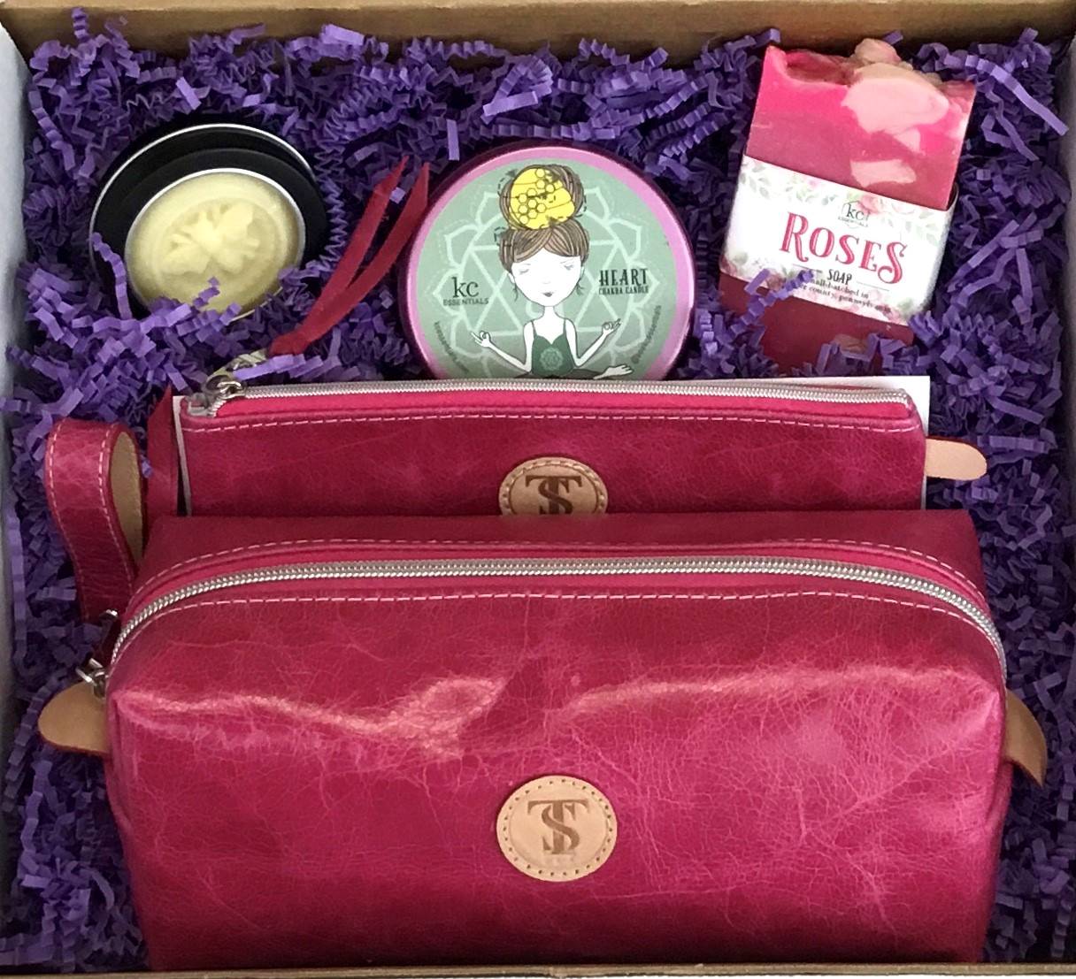 Town & Shore Handcrafted Serenity Gift set featuring T5 Leather bath kit and brush bag shown in dark pink calfskin leather. KC Essentials artisan made vegan bar soap, scented soy chakra candle in a pink metal tin with a lady in a seated yoga pose on lid, and natural solid lotion bar in metal tin. Arranged in gift box with sustainable eco-friendly purple crinkle paper.