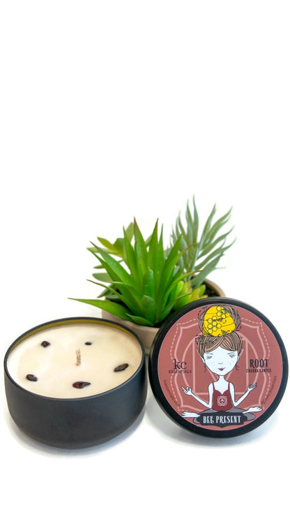 Small plant next to the Scented Root Chakra Candle in matt black  Lidded Tin with Garnet crystals in the soy wax. Lid shows a girl in a seated yoga pose