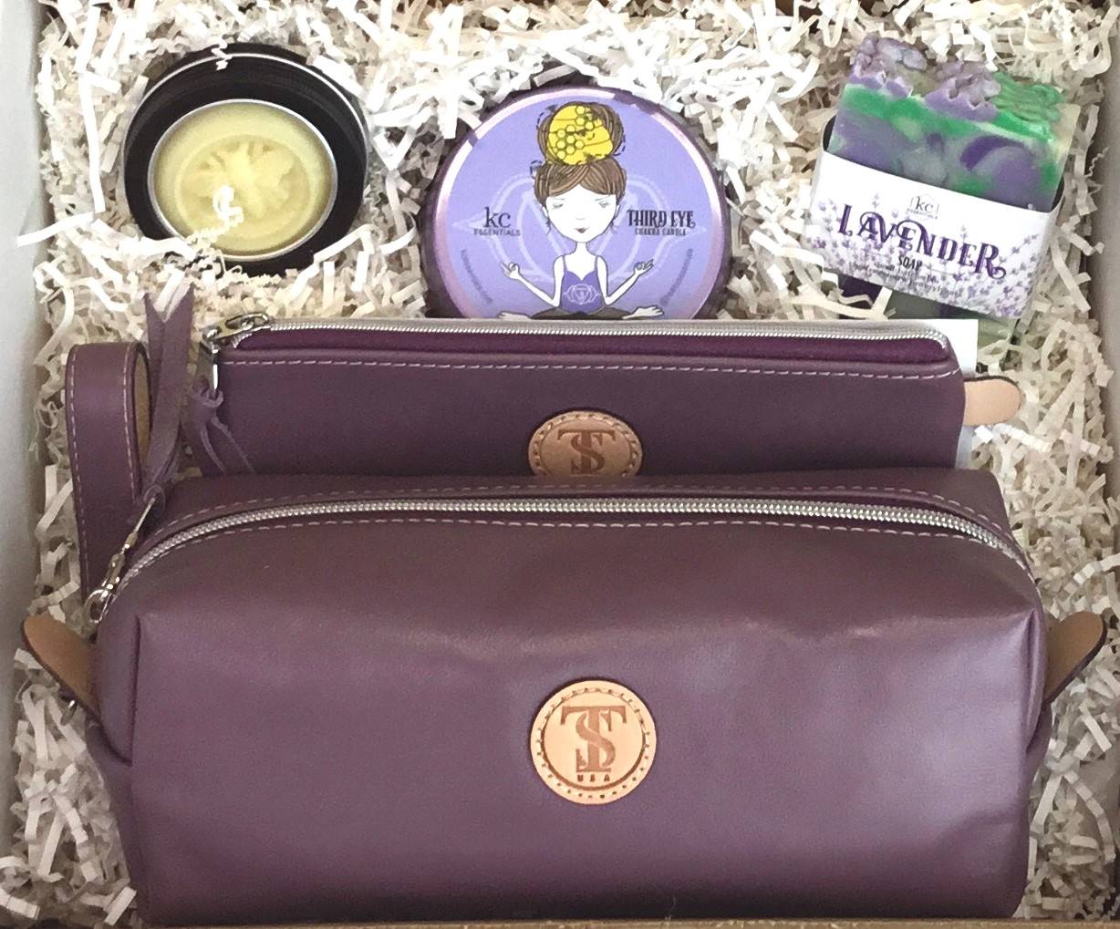 Town &amp; Shore Handcrafted Serenity Gift set featuring T5 Leather bath kit and brush bag shown in Lavender purple calfskin leather. KC Essentials artisan made vegan bar soap, scented soy chakra candle in a purple metal tin with a lady in a seated yoga pose on lid, and natural solid lotion bar in metal tin. Arranged in gift box with sustainable eco-friendly white crinkle paper.