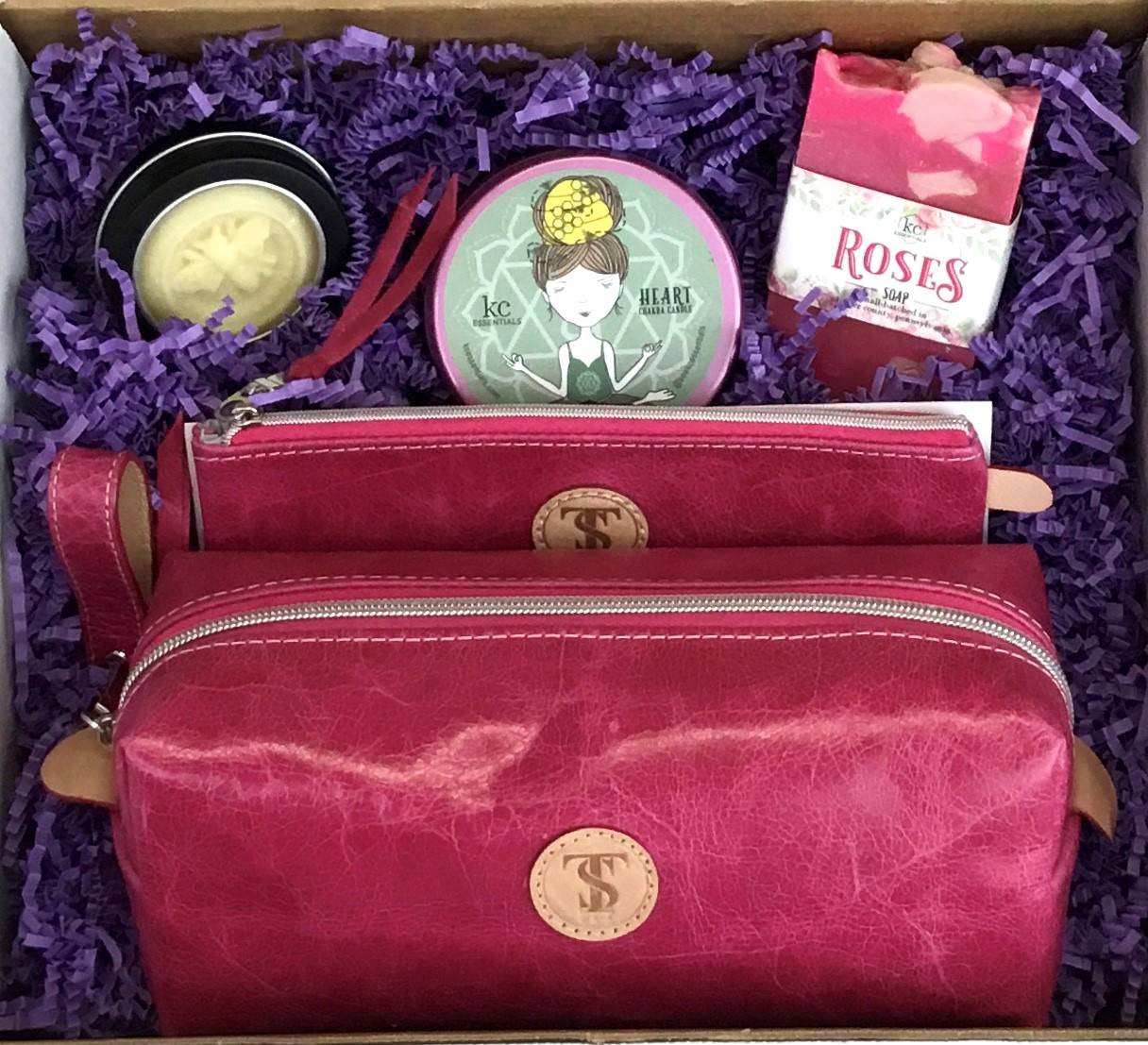 Town &amp; Shore Handcrafted Serenity Gift set featuring T5 Leather bath kit and brush bag shown in dark pink calfskin leather. KC Essentials artisan made vegan bar soap, scented soy chakra candle in a pink metal tin with a lady in a seated yoga pose on lid, and natural solid lotion bar in metal tin. Arranged in gift box with sustainable eco-friendly purple crinkle paper.