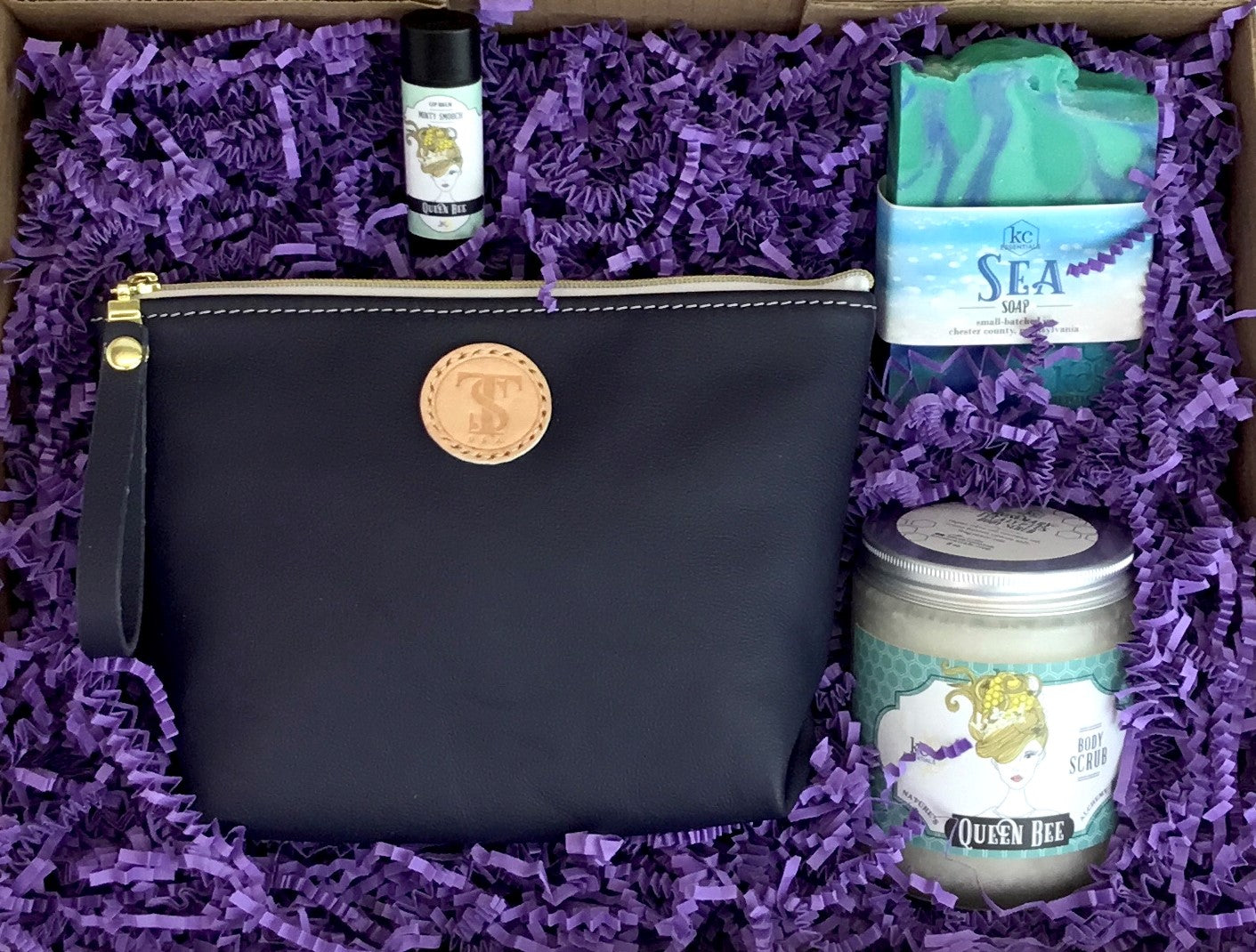 Town &amp; Shore Handcrafted Serenity Gift set featuring T5 Leather bath kit and brush bag shown in navy blue calfskin leather. KC Essentials artisan made vegan bar soap, essential oils body scrub and soothing lip balm. Arranged in gift box with sustainable eco-friendly purple crinkle paper.