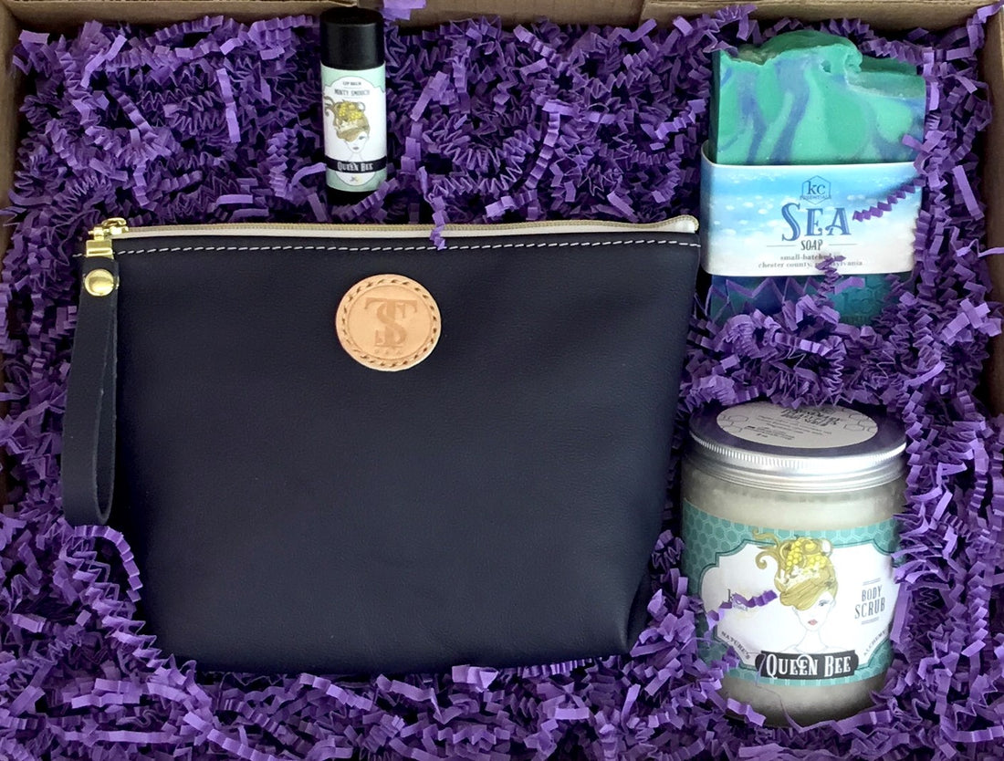 Town &amp; Shore Handcrafted Serenity Gift set featuring T5 Leather bath kit and brush bag shown in navy blue calfskin leather. KC Essentials artisan made vegan bar soap, essential oils body scrub and soothing lip balm. Arranged in gift box with sustainable eco-friendly purple crinkle paper.