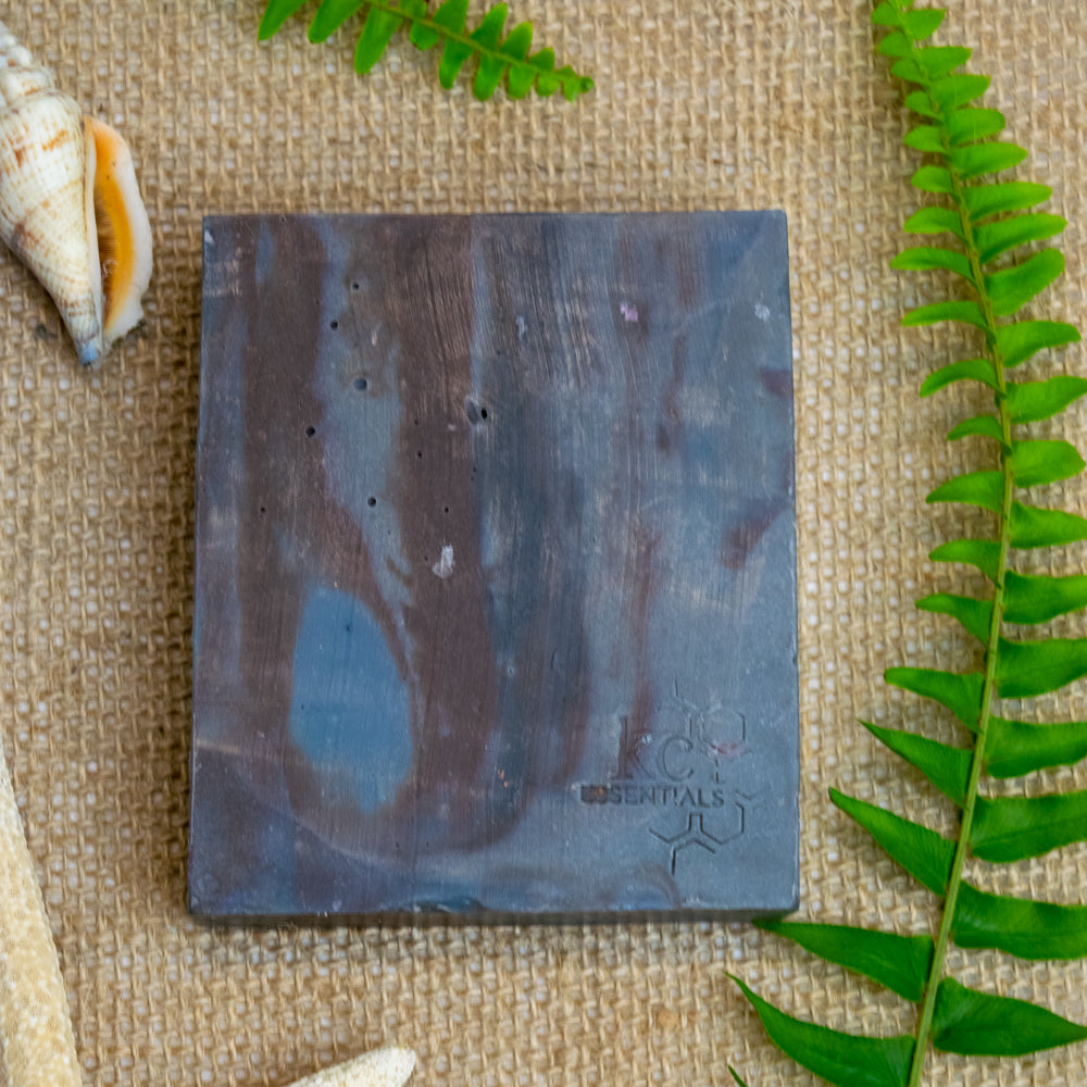 Streaks of brown and shades of grey form this artisanal soap bar on a backrop of burlap cloth with seashells and fern leaves.