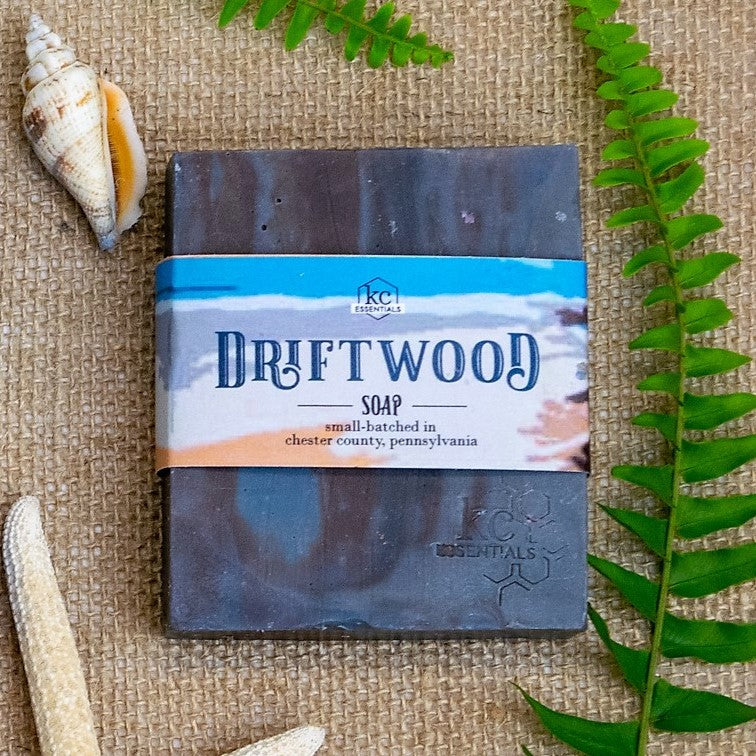 Streaks of brown and shades of grey form this artisanal soap bar on a backrop of burlap cloth with seashells and fern leaves.
