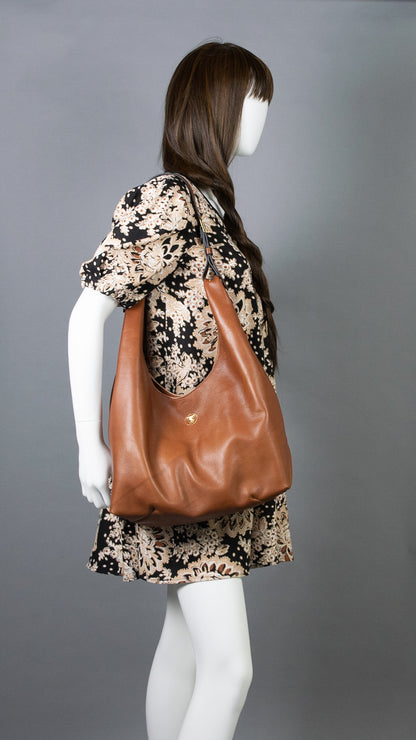 Model with black floral print dress showing Cognac brown leather hobo shoulder bag handcrafted in Italian calfskin by slow fashion indie designer Liv McClintock. Made in Wilmington Delaware USA.