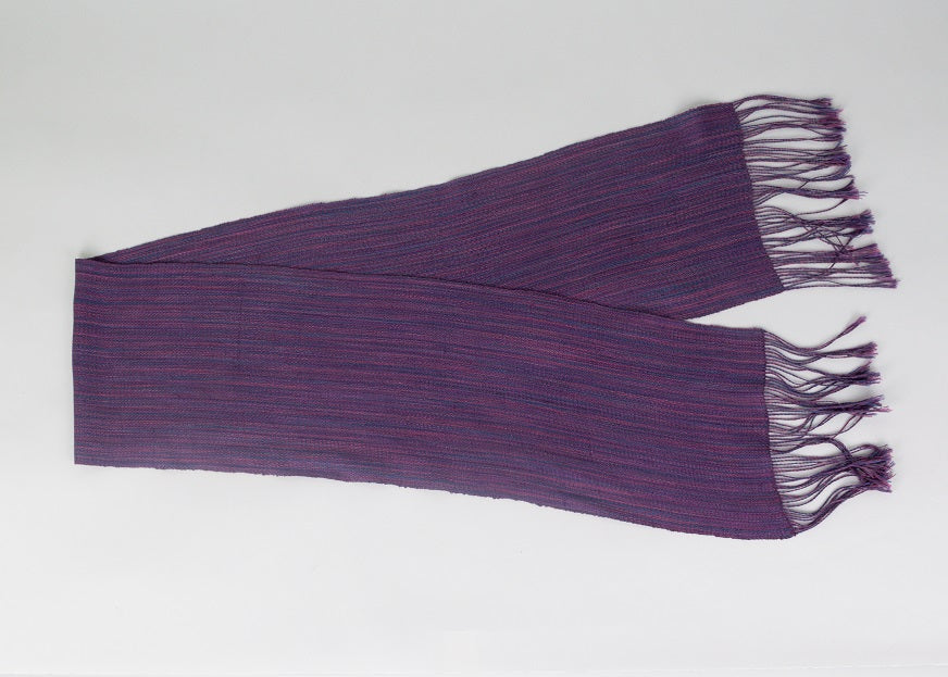 Handwoven scarf laying flat in rich varigated colors of purple, pink and blue with fringe on end